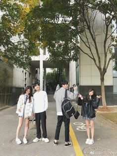 four people standing in front of a building with trees on both sides and one person taking a selfie