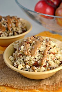 two bowls filled with rice and nuts on top of a yellow towel next to apples