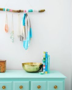 a blue dresser with jewelry hanging from it's sides and a gold bowl on top