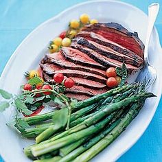 a white plate topped with meat and asparagus on top of a blue table