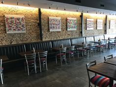 an empty restaurant with tables and chairs lined up against the brick wall that has pictures on it