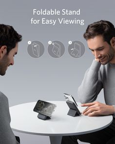 two men are sitting at a table and one is looking at an electronic device while the other looks at it