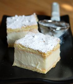 three pieces of cake sitting on top of a black plate next to a silver container