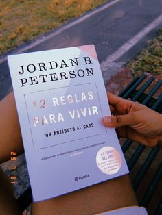 a person sitting on a bench holding up a book in their left hand with the title 12 reglas para vivirr