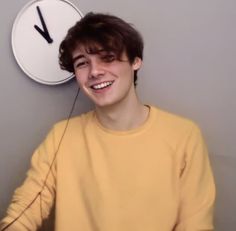 a young man smiling in front of a clock with the time on it's face