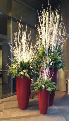 two large red vases with white flowers and greenery in them on the ground