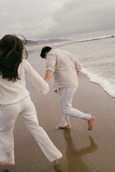 two people running on the beach holding hands