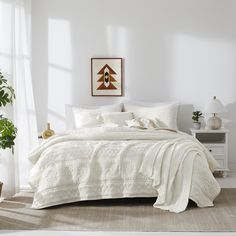 a bed with white linens and pillows in a room next to a potted plant