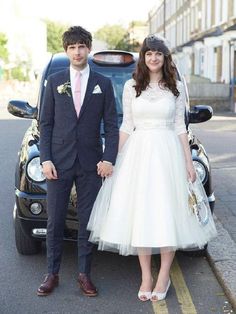 a man and woman in formal wear standing next to a black car on the street