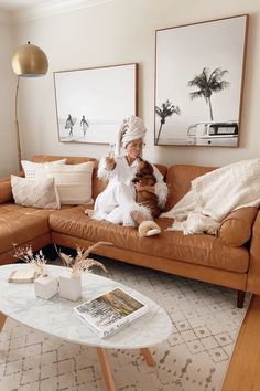 a woman sitting on top of a brown couch in a living room next to a coffee table