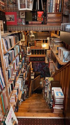 a room filled with lots of books next to a stair case full of books on top of wooden shelves