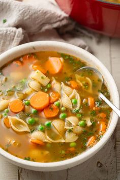 a bowl of pasta and vegetable soup with a spoon in it on a wooden table