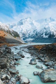 a river running through a rocky valley with snow covered mountains in the background