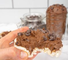 a hand holding a half eaten chocolate dessert in front of a jar of chocolate pudding