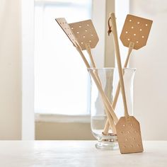 three wooden utensils in a glass vase on a white countertop next to a window