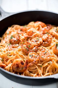 pasta with shrimp and tomato sauce in a skillet on a white wooden table top