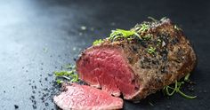 a piece of meat with herbs on it sitting on top of a black table next to another piece of meat