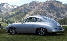 an old silver car parked in front of a mountain