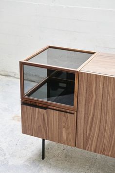 a wooden cabinet with glass top and metal legs on concrete floor next to white wall