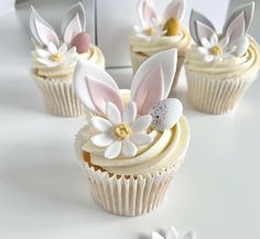 cupcakes decorated with bunny ears and flowers on a white countertop next to two smaller ones