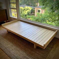 a wooden bed frame sitting on top of a rug in front of a large window