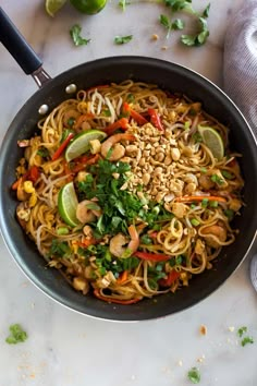 a wok filled with noodles and vegetables on top of a white counter next to limes