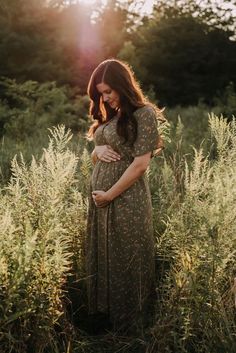 a pregnant woman standing in tall grass at sunset