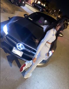 a woman leaning on the hood of a car in front of a black sports car