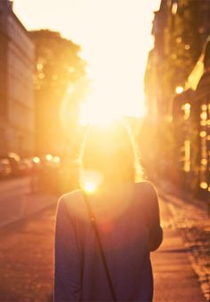 a woman walking down the street at sunset with her back turned to the camera,