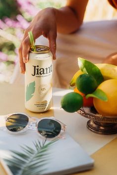 a can of juice sitting on top of a table next to some fruit and sunglasses