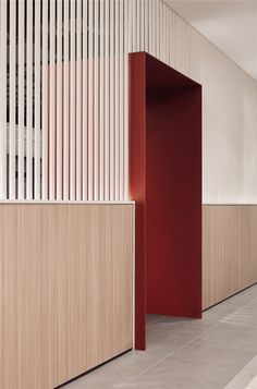 an empty hallway with wooden partitions and red doors on either side, in front of a white wall