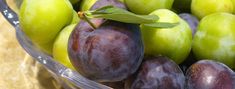 a glass bowl filled with green and purple plums