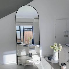 a mirror sitting on top of a white floor next to a vase filled with flowers