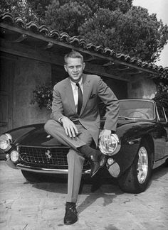 a black and white photo of a man sitting on the hood of a sports car