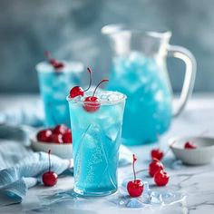 two glasses filled with blue liquid and cherries on the rim, next to ice