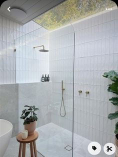 a white tiled bathroom with a wooden stool next to the walk in shower and potted plant