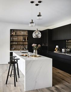 a kitchen with black cabinets and white marble counter tops, two pendant lights hanging from the ceiling