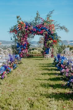 an outdoor ceremony set up with white chairs and colorful flowers on the arch over looking the ocean