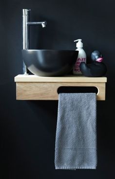 a bathroom sink sitting on top of a wooden shelf next to a towel and soap dispenser