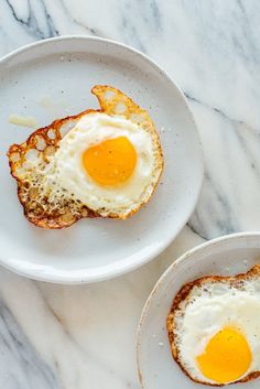 two white plates topped with eggs and toast on top of a marble countertop next to each other