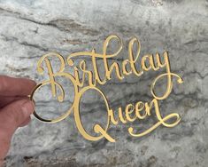 a hand holding a birthday queen cutout on top of a marble slab with the words'birthday queen'in gold foil