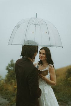 a bride and groom standing under an umbrella in the rain on their wedding day, looking at each other