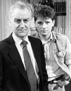 two men standing next to each other in front of a bookshelf