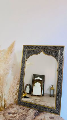 a mirror sitting on top of a wooden table next to a vase with dry grass