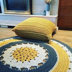 a crocheted round rug on the floor next to two pillows and a mirror