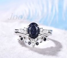 a fancy ring with a blue stone surrounded by white and black diamonds on a light blue background