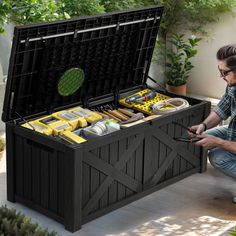 a man sitting on the ground next to an outdoor storage box filled with tools and supplies