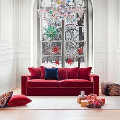 a red couch sitting in front of a large window next to a christmas decoration on the wall