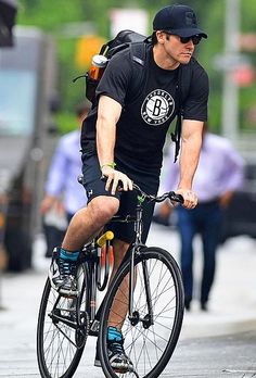 a man is riding his bike down the street with an umbrella over his head and wearing a black hat