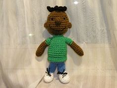 a crocheted stuffed animal wearing a green shirt and blue pants